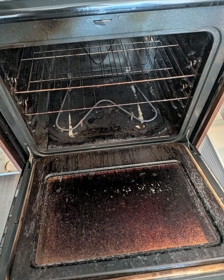 Open oven with burnt grease across the floor and around the racks
