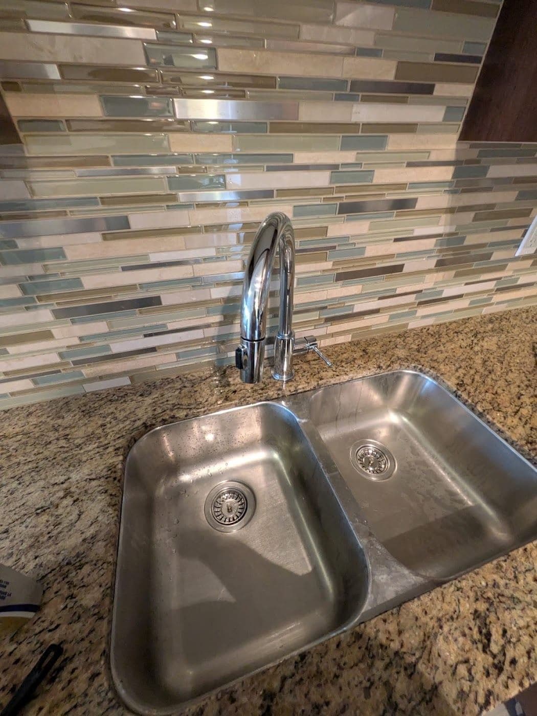 A stainless steel double sink under a glass tile backsplash