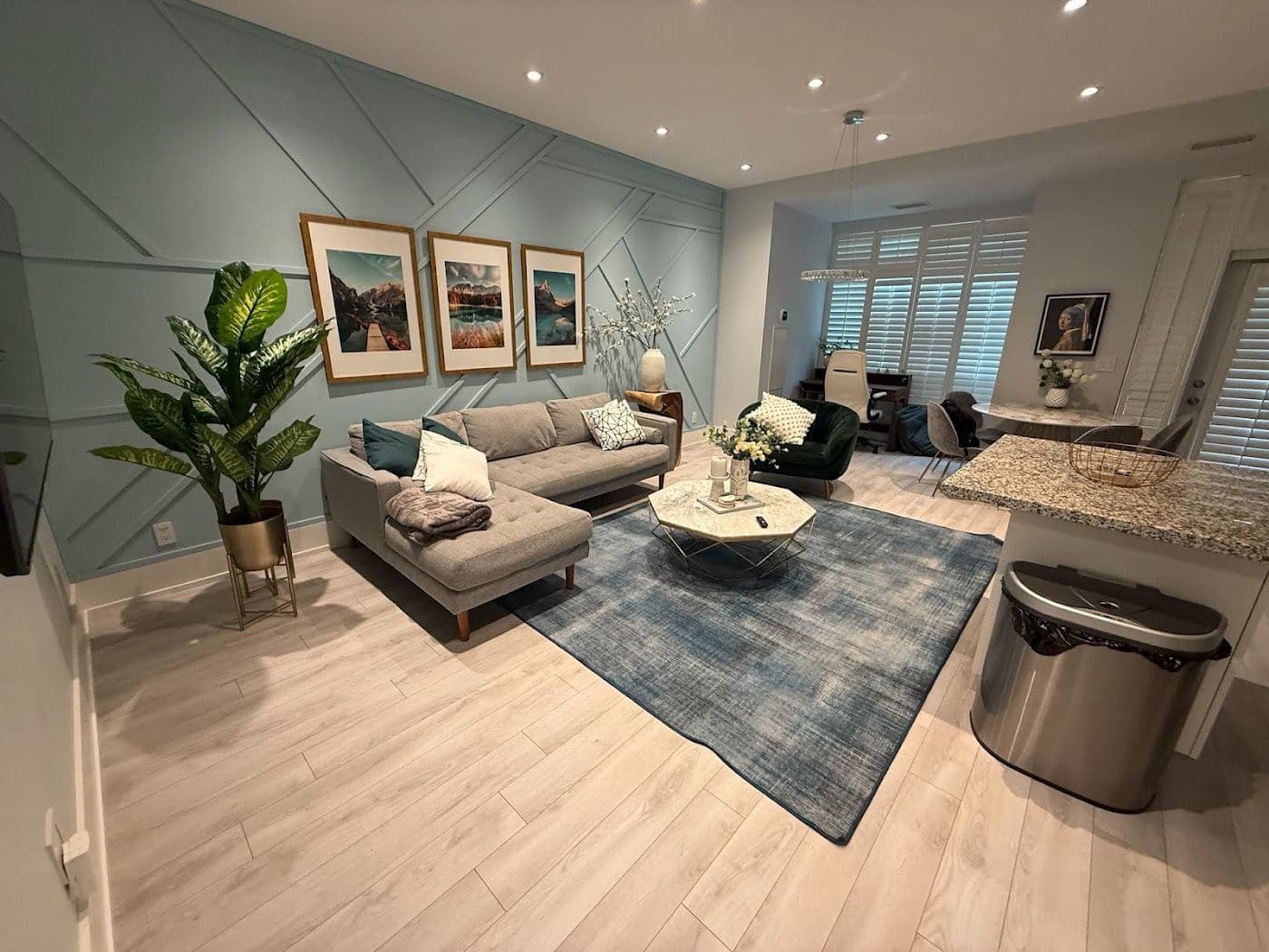 A living room with a grey sectional, three framed prints, a tall plant and a blue rug